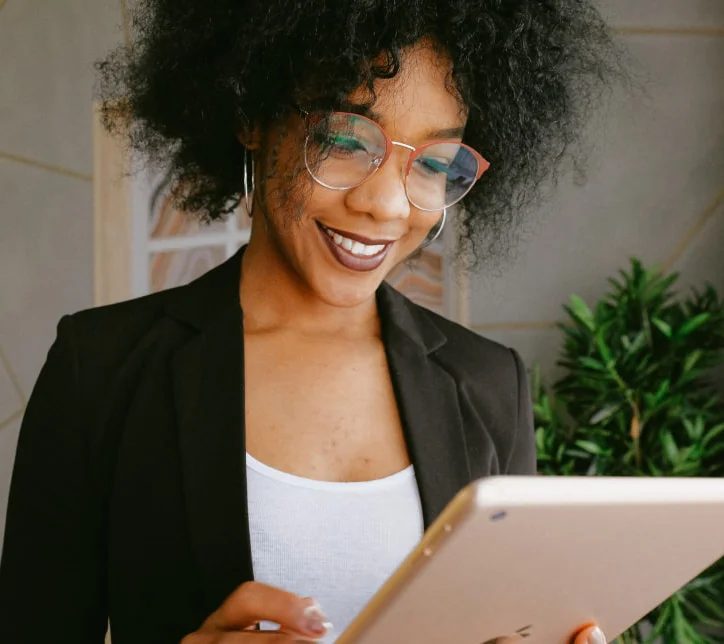 A woman wearing glasses and a black jacket is engaged with an iPad, symbolizing the Digital Communities Program setup process.